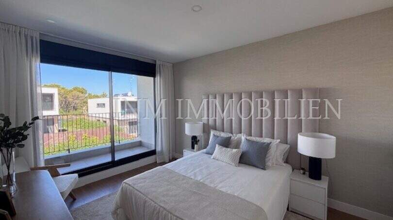 Dormitorio luminoso con cabecero acolchado, ropa de cama blanca y gran ventanal panorámico con balcón en la nueva construcción Puig de Ros