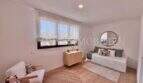 Habitación infantil luminosa con cama nido, cómoda de madera, espejo redondo y moderno suelo laminado en la casa de nueva construcción Puig de Ros.