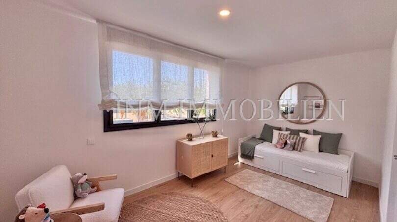 Habitación infantil luminosa con cama nido, cómoda de madera, espejo redondo y moderno suelo laminado en la casa de nueva construcción Puig de Ros.