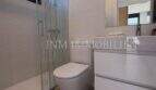Cuarto de baño moderno con ducha de cristal, inodoro suspendido en pared y lavabo blanco en la casa de nueva construcción Puig de Ros