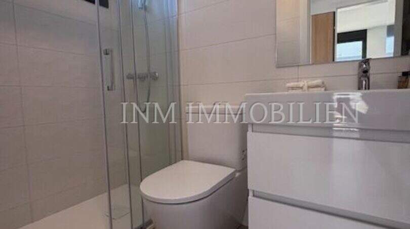 Cuarto de baño moderno con ducha de cristal, inodoro suspendido en pared y lavabo blanco en la casa de nueva construcción Puig de Ros