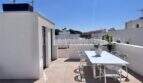 Terraza en la azotea soleada con conjunto de comedor blanco y vista de los alrededores en la casa de nueva construcción Puig de Ros