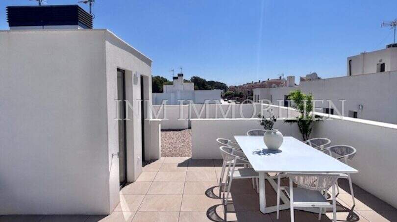 Terraza en la azotea soleada con conjunto de comedor blanco y vista de los alrededores en la casa de nueva construcción Puig de Ros
