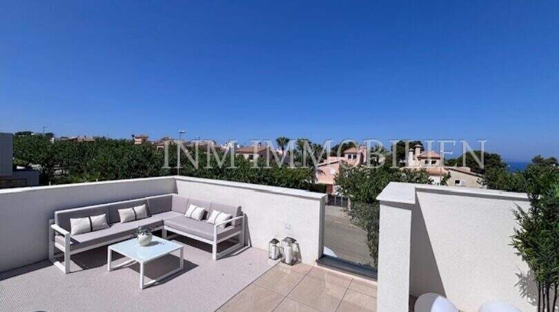 Terraza en la azotea soleada con muebles lounge, vistas al mar y cielo azul radiante en Puig de Ros, Mallorca.
