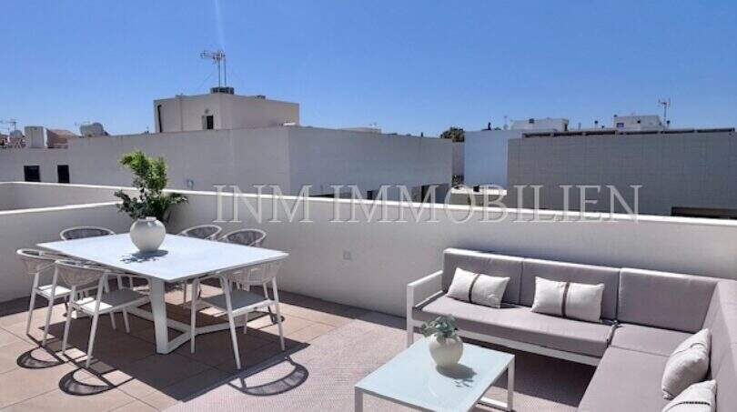 Terraza en la azotea soleada con muebles de exterior blancos, zona lounge y mesa de comedor, casa de nueva construcción en Puig de Ros, Mallorca.
