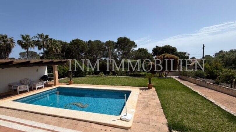 Gepflegter Außenbereich des Chalets in Cala Pi mit rechteckigem Pool, Terrasse und grünem Garten mit Palmen.