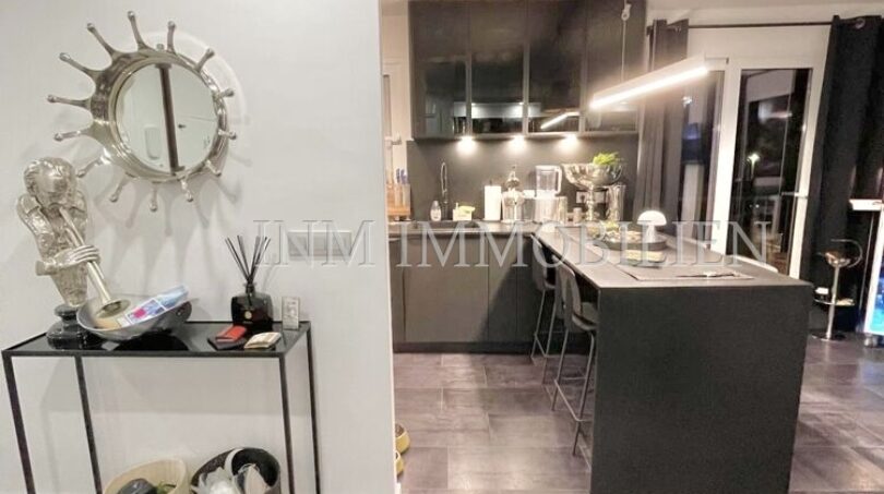 Modern living kitchen area with dark kitchen island, bar stools, designer mirror and stone tile floor in sea view apartment Palma