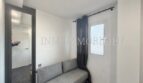 Small room with gray sofa, window with dark curtain and large wall mirror in sea view apartment Palma