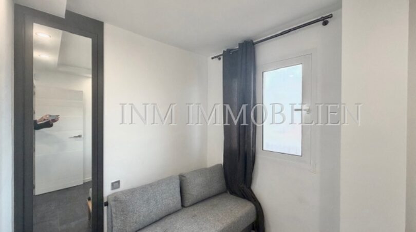 Small room with gray sofa, window with dark curtain and large wall mirror in sea view apartment Palma