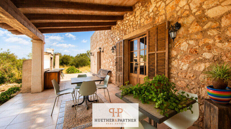 Überdachte Terrasse der Finca mit Natursteinwand, Holzbalkendecke, Sitzbereich und mediterranem Ausblick