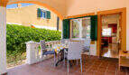 Überdachte Terrasse mit Esstisch, Rattanstühlen und grünen Fensterläden am Doppelhaus in Cala Murada