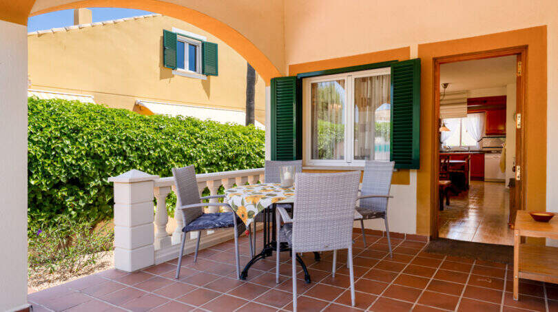 Überdachte Terrasse mit Esstisch, Rattanstühlen und grünen Fensterläden am Doppelhaus in Cala Murada