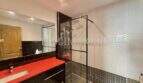 Moderno cuarto de baño con ducha tipo walk-in, encimera de lavabo roja y azulejos negros en apartamento en Palma.