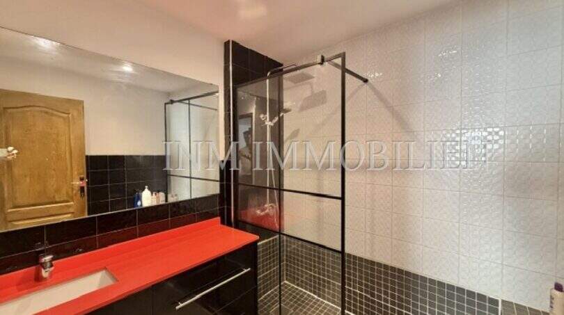 Moderno cuarto de baño con ducha tipo walk-in, encimera de lavabo roja y azulejos negros en apartamento en Palma.