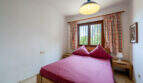 Dormitorio de la villa de Cala Murada con cama de matrimonio, muebles de madera y cortinas de colores en la ventana enrejada.