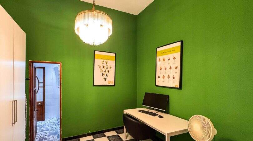 Arbeitszimmer mit grünen Wänden, Kronleuchter, weißem Schreibtisch und Weinposter in Felanitx