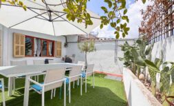 Sonnige Terrasse mit weißen Gartenmöbeln, Sonnenschirm, Kunstrasenfläche und Kaktuspflanzen in Felanitx