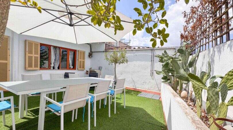 Sonnige Terrasse mit weißen Gartenmöbeln, Sonnenschirm und Kakteen in Felanitx