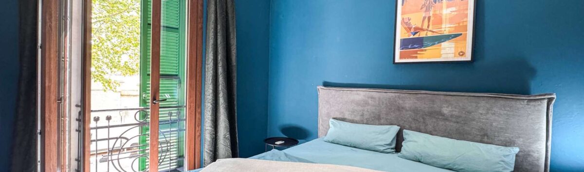 Bedroom with a blue wall, a double bed, a balcony with green shutters, and a Mallorca poster in Felanitx