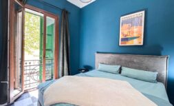 Dormitorio con pared azul, cama doble, balcón con contraventanas verdes y póster de Mallorca en Felanitx.