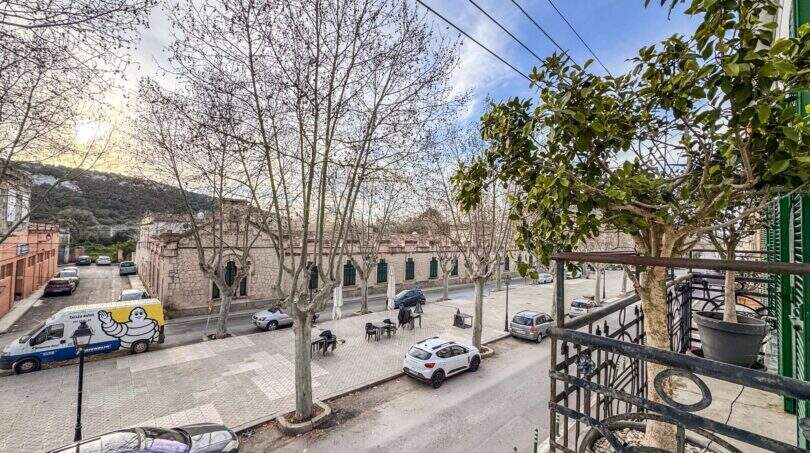 Blick vom Balkon auf den belebten Stadtplatz von Felanitx mit kahlen Platanen und historischen Steingebäuden.