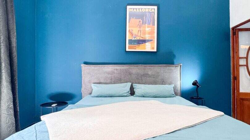 Schlafzimmer mit Doppelbett, blauer Akzentwand und Mallorca-Poster in stilvoller Wohnung in Felanitx