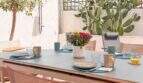 Gedeckte Außenterrasse mit grauem Esstisch, blauen Platzsets, Blumendeko und Kaktus in Felanitx