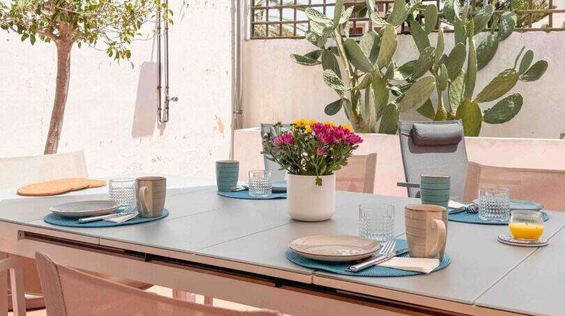 Gedeckte Außenterrasse mit grauem Esstisch, blauen Platzsets, Blumendeko und Kaktus in Felanitx