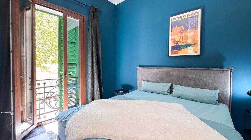 Stilvolles Schlafzimmer mit blauer Wandfarbe, Doppelbett, Balkon und Mallorca-Poster in Felanitx