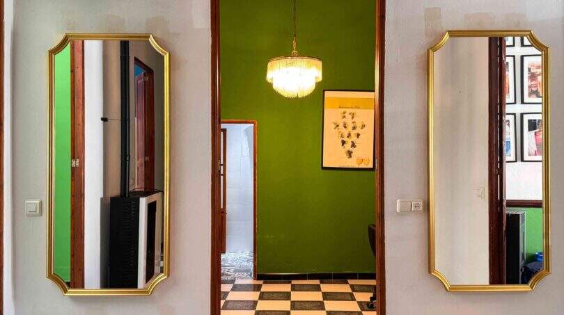 Flur mit zwei goldgerahmten Wandspiegeln, Kristallleuchter und markanter grüner Wand in stilvoller Wohnung Felanitx
