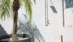 Außendusche mit Kupferrohren an weißer Wand, Palme im Topf und Kunstrasenfläche in Felanitx