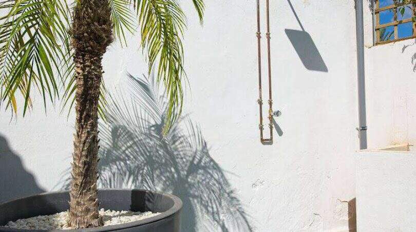 Außendusche mit Kupferrohren an weißer Wand, Palme im Topf und Kunstrasenfläche in Felanitx