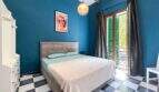 Schlafzimmer mit blauer Wand, Doppelbett, Schachbrettboden und Balkon mit grünen Fensterläden in Felanitx