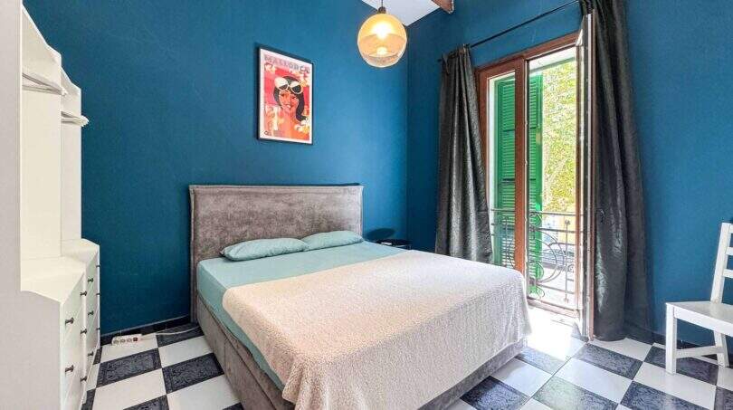 Schlafzimmer mit blauer Wand, Doppelbett, Schachbrettboden und Balkon mit grünen Fensterläden in Felanitx