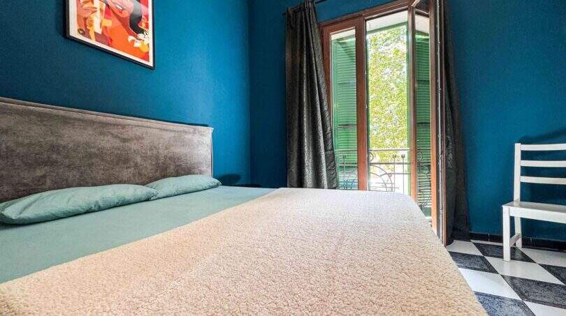 Schlafzimmer mit Doppelbett, blauer Wand, Balkon mit grünen Fensterläden und Schachbrettboden in Felanitx