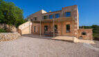 Außenansicht einer rustikalen Sandstein-Finca mit überdachter Terrasse, Außenkamin und Kiesvorplatz in Cales de Mallorca.