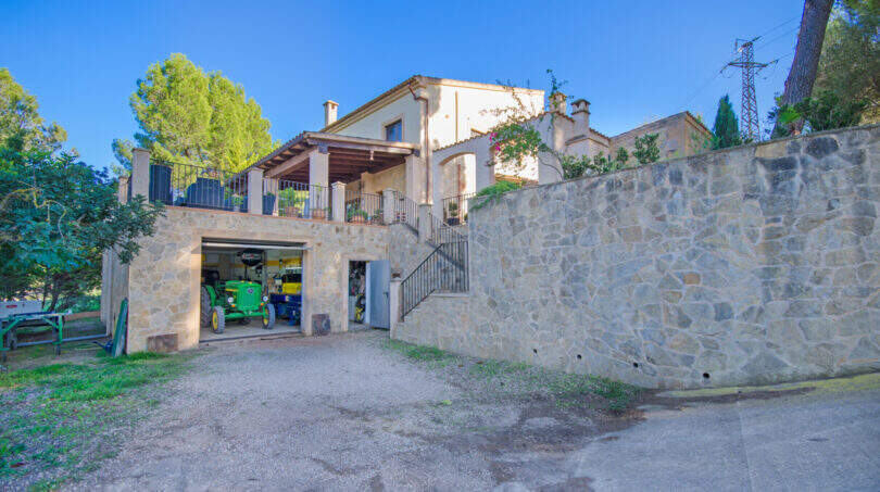 Finca Son Macià: Steingebäude mit Garage, John Deere Traktor, Balkon und großer Natursteinmauer im Außenbereich.