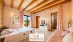 Helles Schlafzimmer der Finca Felanitx mit Holzbalkendecke, rosa Akzenten und En-Suite-Bad