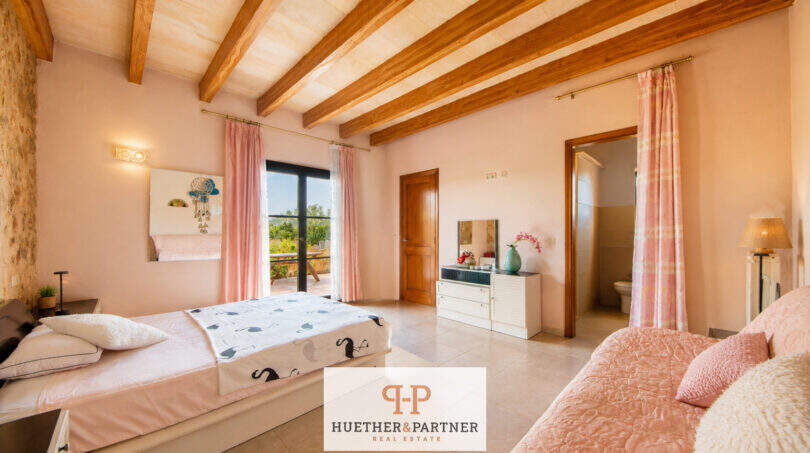 Helles Schlafzimmer der Finca Felanitx mit Holzbalkendecke, rosa Akzenten und En-Suite-Bad