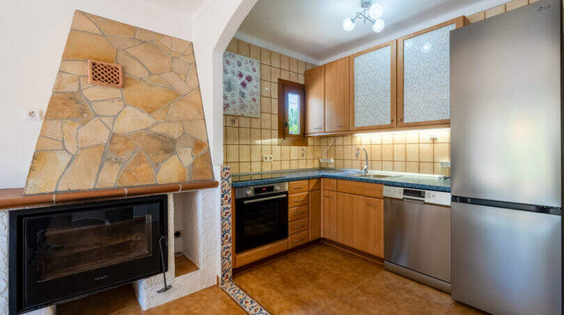 Küche mit Holzschränken, Steinverkleidung, Kamin, Edelstahlkühlschrank und Fliesenspiegel in Cala Murada