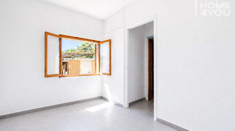 Helles, leeres Zimmer mit Holzfenster, weißen Wänden und Fliesenboden in Erdgeschosswohnung, Cala Llombards