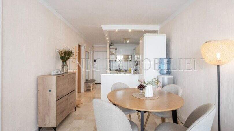 Comedor luminoso con mesa de madera redonda, sillas modernas y cocina abierta en apartamento en Port Adriano, Calvià.