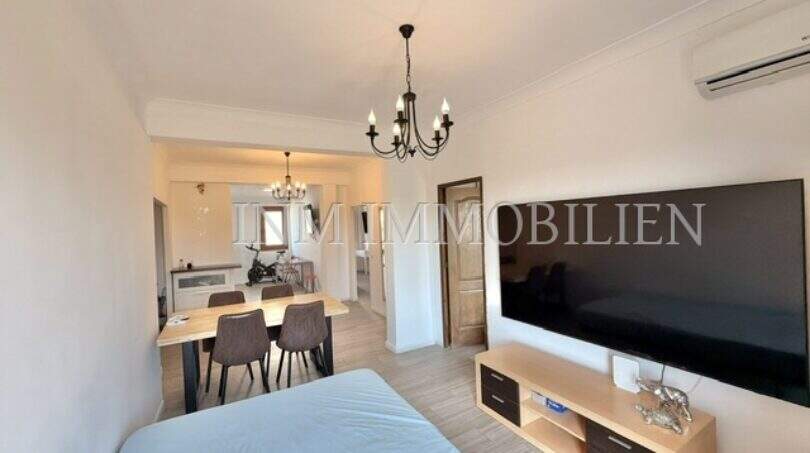Luminoso salón con gran televisor, mesa de comedor y lámpara de araña en apartamento renovado en Palma