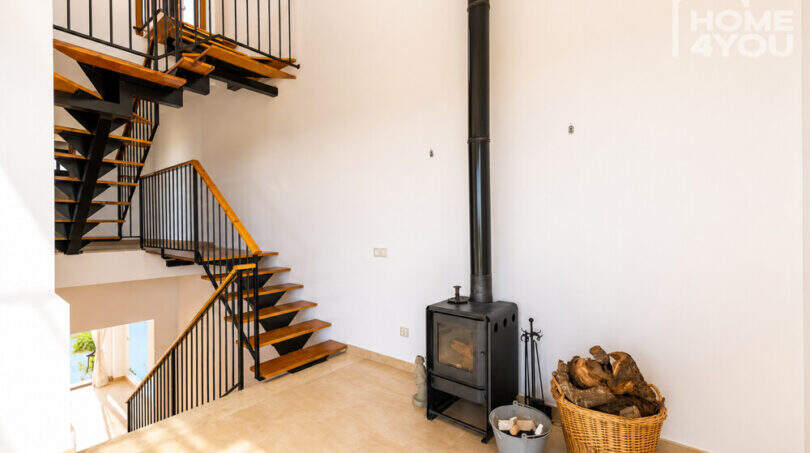 Wohnbereich mit moderner Stahltreppe, Holzstufen und schwarzem Kaminofen mit Holzkorb in Ses Salines