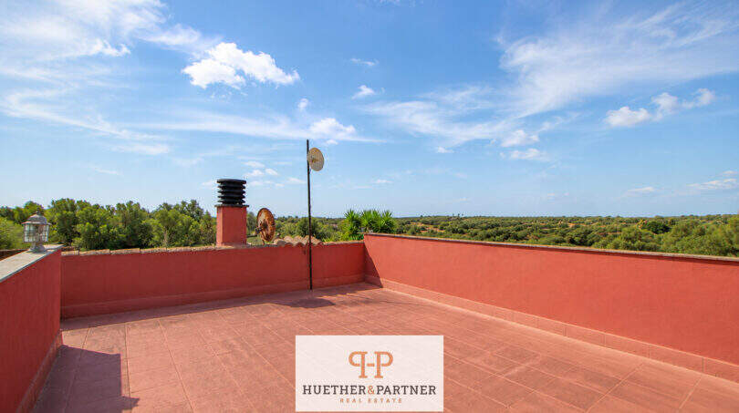 Dachterrasse der Finca bei Felanitx mit rotem Mauerwerk, Antennen und weitem Blick über grüne Landschaft unter blauem Himmel