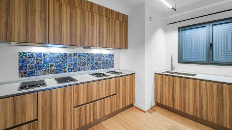 Moderne Küche der Luxuswohnung am Paseo Marítimo mit Holzfronten, weißer Arbeitsfläche und bunten Mosaikfliesen.