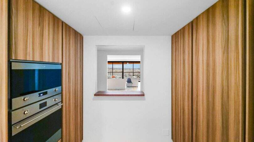 Moderne Küche mit Holzfronten und Einbauofen, Durchreiche mit Meerblick, Luxuswohnung Palma