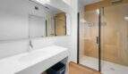 Modernes Badezimmer der Luxuswohnung am Paseo Marítimo mit Glasdusche, weißem Waschtisch und Holzboden.
