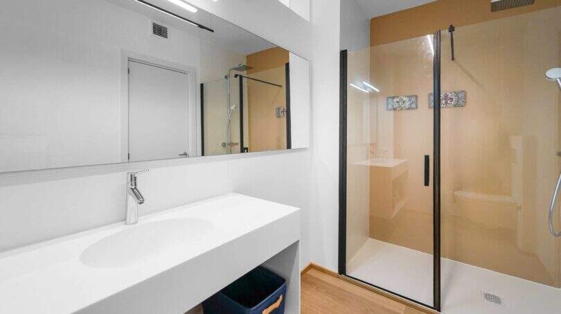 Modernes Badezimmer der Luxuswohnung am Paseo Marítimo mit Glasdusche, weißem Waschtisch und Holzboden.
