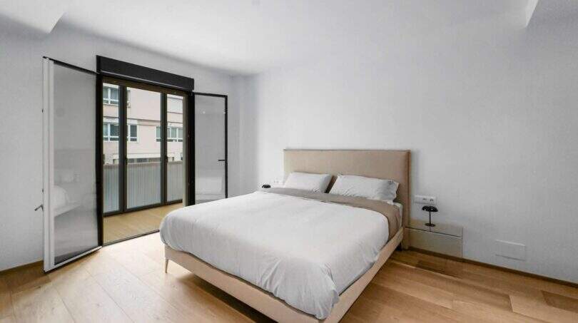 Helles Schlafzimmer der Luxuswohnung am Paseo Marítimo mit Doppelbett, Holzboden und Balkonzugang.